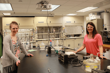 Two girls standing in a chemistry classroom. 