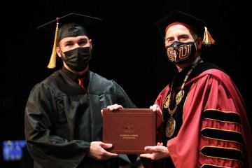 A student grabbing his diploma on stage during graduation.