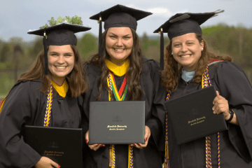 Three girls in graduation gowns and caps, holding diplomas. 