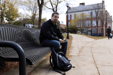 A man sitting on a bench with his backpack. 