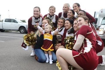 A cheer group kneeling next to a toddler wearing a cheer outfit. 