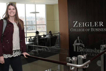 A woman standing next to a sign that says Ziegler College of Business. 