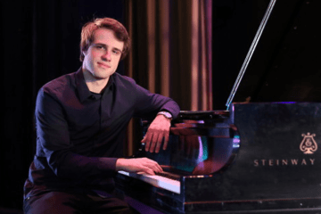 A man sitting by a piano. 