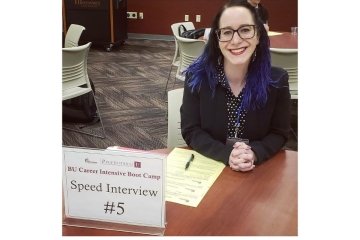 A woman leaning on a desk with a speed interview sign. 