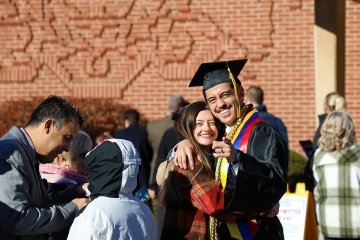 A guy and a girl hugging in a graduation gown and cap.