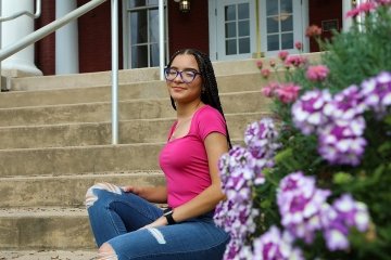 A girl in a pink top and jeans sitting on a staircase. 