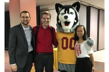 Three people standing with a husky mascot.