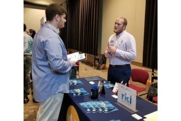 A man talking to a man behind a vendor table.