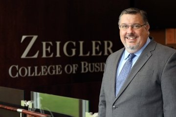 A man standing next to a Ziegler College of Business sign. 