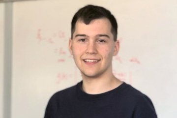 A man in a black shirt with a white board behind him. 