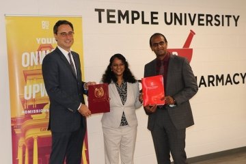 Three people standing side by side in front of a Temple University sign. 