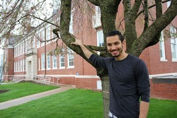 A man standing by a tree in front of a building. 