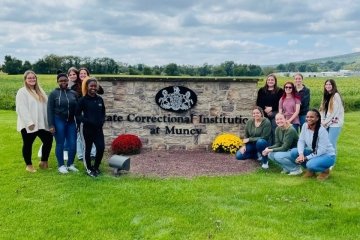 Two groups on wither side of a flower bed and a wall that says: State Correctional Institute