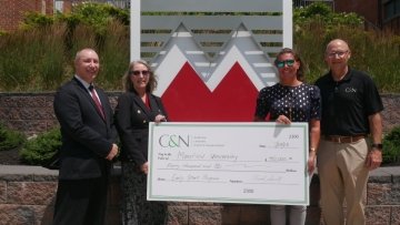 Four people standing around a giant C&N check. 