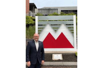 A man standing in front of a Mansfield logo sign. 