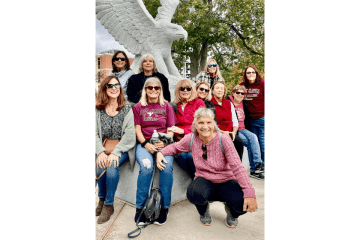 A group of alumni sitting by the bald eagle mascot statue. 