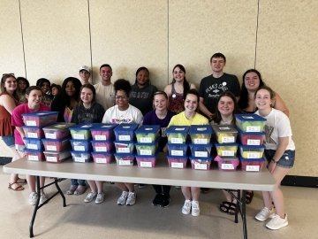 A group of students standing behind a table with boxes on it. 