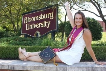 A girl sitting on a ledge by a Bloomsburg University Sign. 