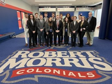 Group of people standing on a floor that says: Robert Morris Colonials 