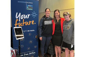 Three people standing side by side next to a your future sign. 