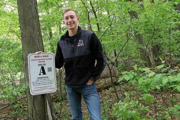 A man standing next to a sign next to a tree. 