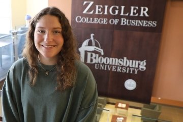 A girl standing in front of a Zeigler College of Business sign. 