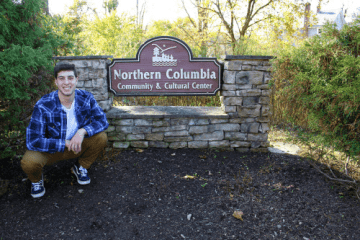 A man kneeling next to a sign outside. 