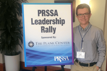 A man standing next to a PRSSA Leadership Rally sign.