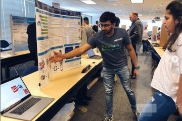 A man looking at a computer and an information board. 