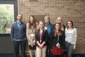 A group of people standing together in front of a brick wall. 