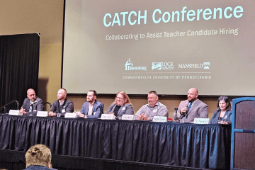 A group of people sitting at a table with a smart board that says CATCH Conference