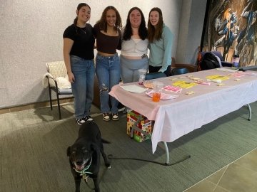 A dog and a group of girls standing behind a table. 