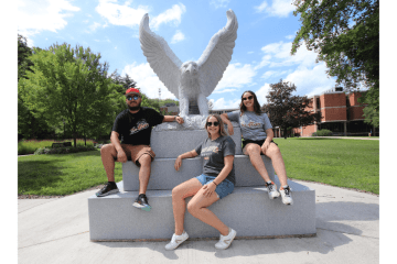 Three people sitting around an eagle statue. 