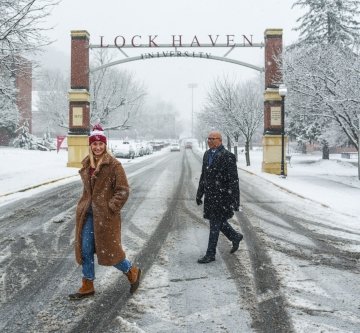 Two people walking across the road in the snow. 