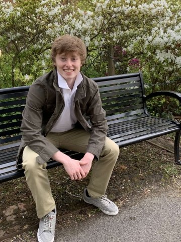 Carson sitting on a bench in front of some greenery. 