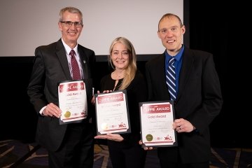 A group of three standing with awards. 