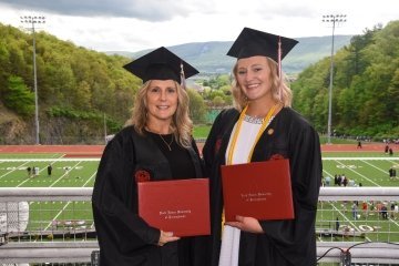 Two women standing together in their graduation caps and gowns with their diplomas. 