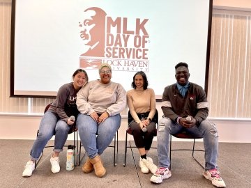 A group of people sitting side by side in front of an MLK Day of Service Sign. 