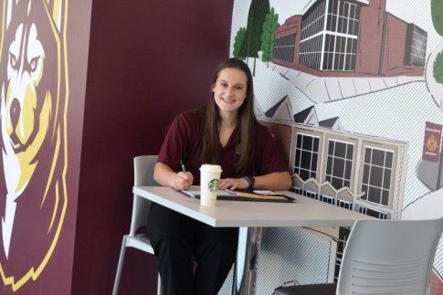 a photo of angela dipasquale sitting in a dining hall doing work and smiling