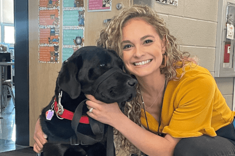 a photo of Alexis Saxton smiling with a black lab dog