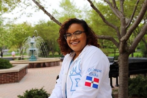 Sheira Sosa outside on a bench in front of a fountain, smiling.