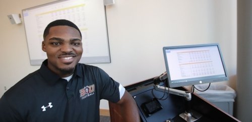 a Black MBA student smiling next to a computer with a presentation in the background