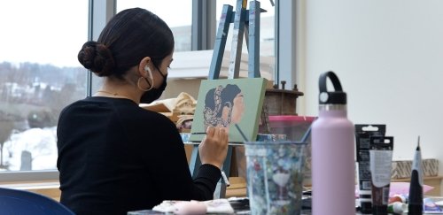 Student paining a picture with airpods in and a face mask on: a painting with a snake around a head