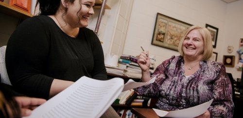 English major and professor talking and laughing while reviewing papers