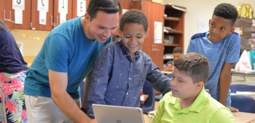 a student teacher working with a group of kids around a computer