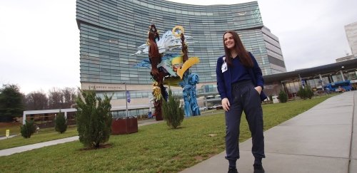 a student standing in front of a children's hospital smiling