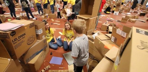 Two female Commonwealth University students build cardboard fort with young child.