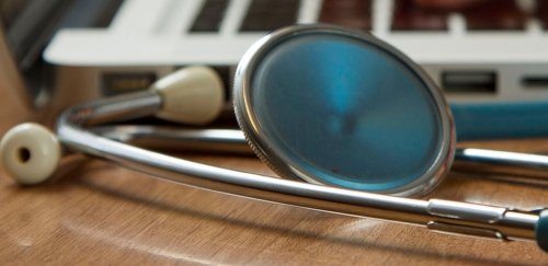 A stethoscope laying on a desk near a laptop.