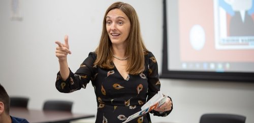 a teacher in front of a projector screen, pointing and looking off into the distance