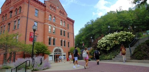 Undergraduate college students walk across the campus of Commonwealth University-Mansfield, formerly Mansfield University of Pennsylvania, with North Hall in the background